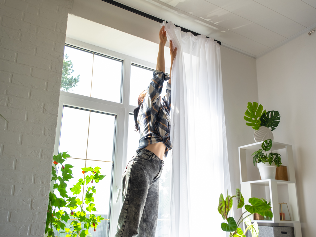 A person holding a curtain, hanging curtains is just one way to reduce energy costs, there are other things you can do and we discuss this in this blog.