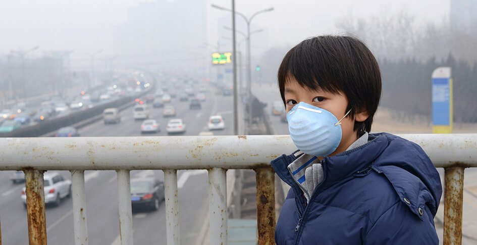 Boy wearing a mask on a balcony with smog in the background.