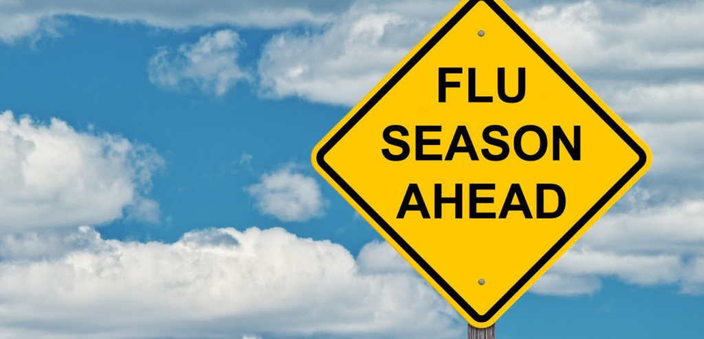 A yelllow caution sign stating Flu Season ahead with blue cloudy sky background