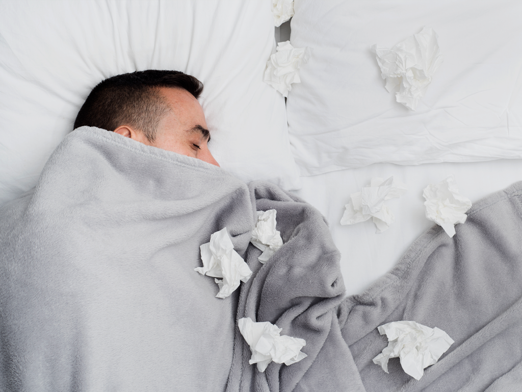 A man in bed covered up with used tissue around him, the flu season is upon us with plenty of sick days.