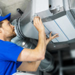 An HVAC Technician maintaining an HVAC system, maintenance is key to bring building up to clean air standards.