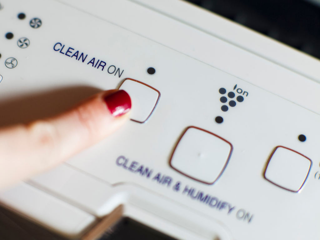 Womans finger touching the on button of a white air purifier and ionizer