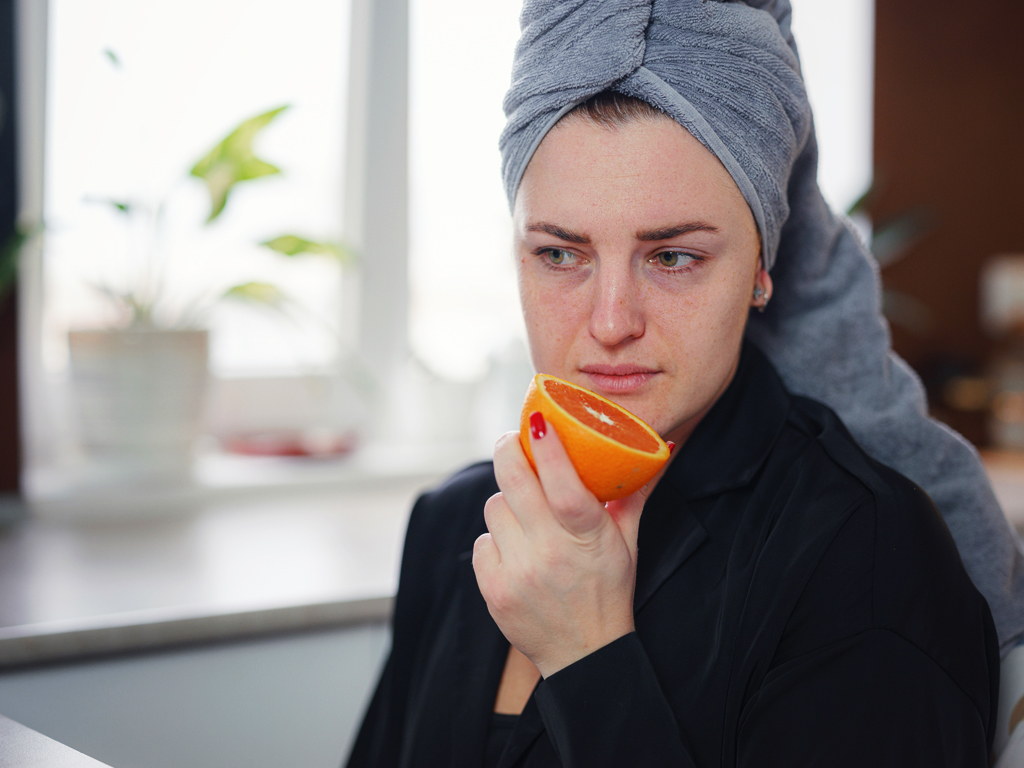 Sick woman trying to smell an orange, loss of smell is a symptom associated with long covid. 