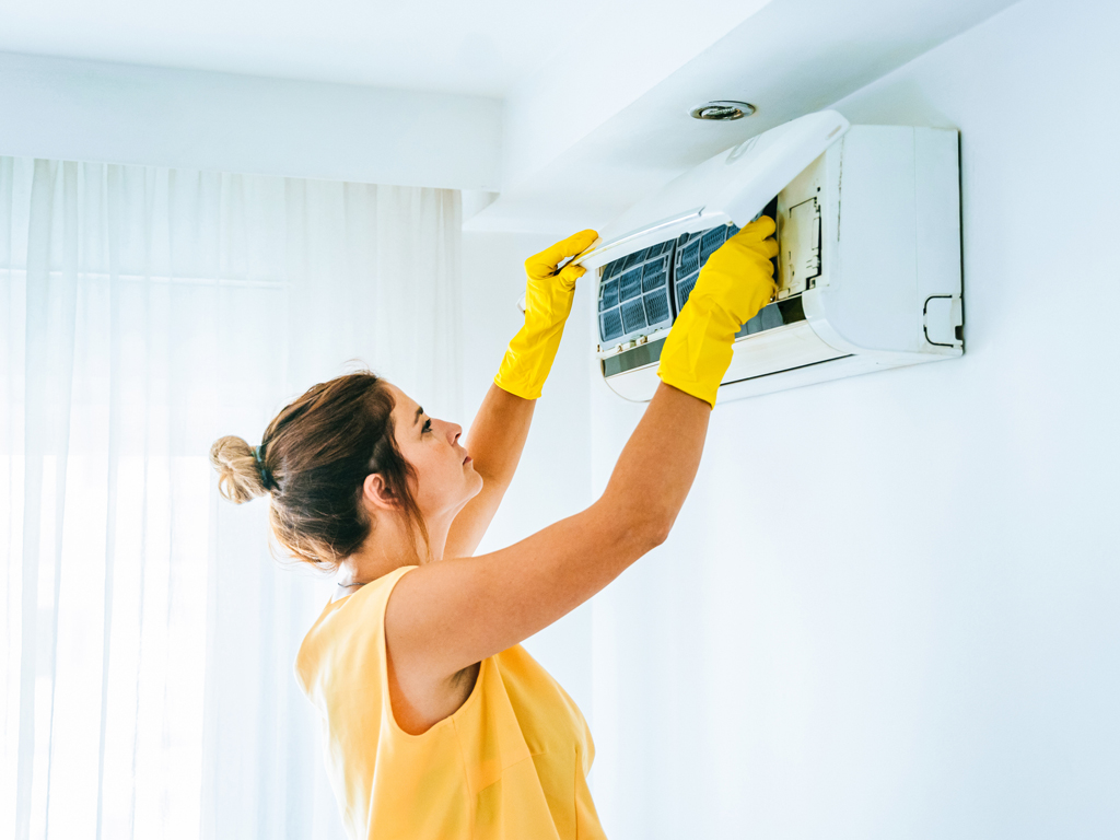 Woman Replacing filter in an Air Conditioning, replacing filters is not the only thing that needs to be done to improve indoor air quality.