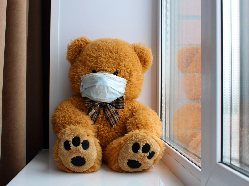A teddy bear sitting on a windowsill with a mask on.